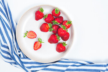 Flat plate full of fresh strawberries. Fresh ripe red strawberry background. Seasonal harvest of strawberries on a white plate and a blue towel. Top view, copy space