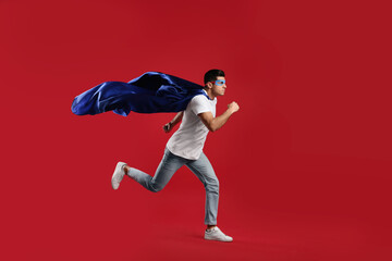 Man in superhero cape and mask running on red background