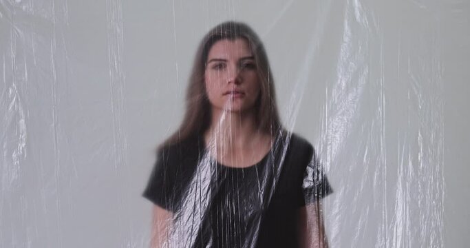 Woman rights. Gender equal. Social isolation. Sad depressed girl victim behind defocused transparent polyethylene film on light out of focus background.