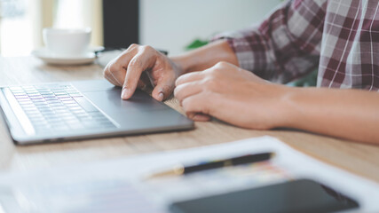 Close-up businessman holding a pen, smartphone and pointing at financial graph checking business report on wooden desk with computer laptop besided at home. Stock photo