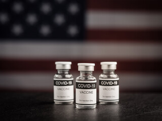 COVID-19 vaccine bottles against the background of the United States flag. Vaccine for immunization, and treatment from coronavirus infection. Close-up photo. Concept of medical and healthcare