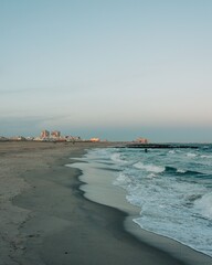 A beach with waves and buildings in the distance, Rockaways, Queens, New York City