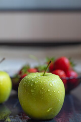 Green apples with drops of water and juicy strawberries in the background