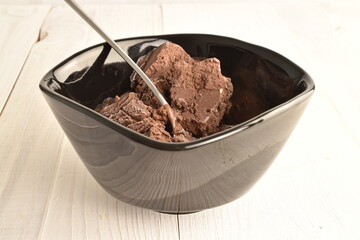 Chocolate sweet ice cream in a black ceramic bowl, close-up, on a wooden table.