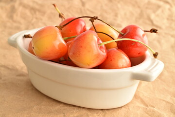 Juicy sweet yellow cherries on a white ceramic dish, close-up, on craft paper.