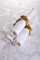 Napkins made of cotton with rings made of yellow metal.Festive table setting.The concept of holidays.Top view.White tablecloth with a textured pattern.Top view.VIP-hall.