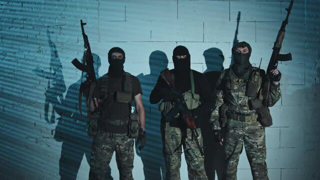 Portrait dolly-in shot of three armed terrorists in balaclavas posing for camera in their hideout