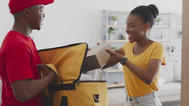 Home delivery service. Black male courier taking box out of bag and giving order to positive african american lady