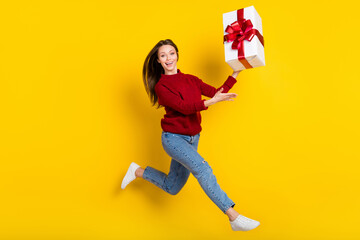 Full length profile photo of sweet millennial lady jump with present wear sweater jeans isolated on vivid yellow color background