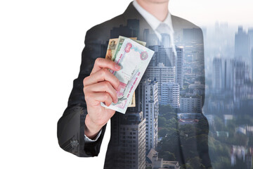 Double exposure of businessman hold United Arab Emirates Dirham (AED) money and cityscape in the foggy morning as business, trade, investment and income concept