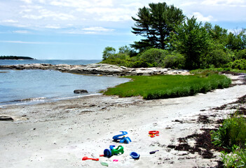 Summertime scene in coastal Maine. Colorful children's toys abandoned on deserted sand beach in Clark Island, Maine.