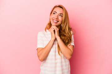 Caucasian blonde woman isolated on pink background keeps hands under chin, is looking happily aside.