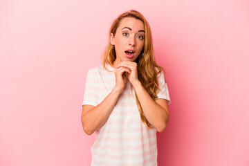 Caucasian blonde woman isolated on pink background praying for luck, amazed and opening mouth looking to front.