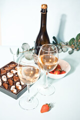 Glasses of champagne or white grape wine with plate of chocolates and strawberry, bottle on the...