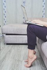 Close-up of the legs of a barefoot woman using a computer on her sofa at home.