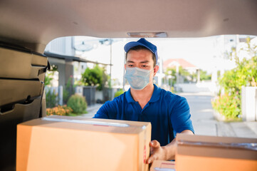 Asian delivery young man wear face mask picking up package carton in hatchback car of van.