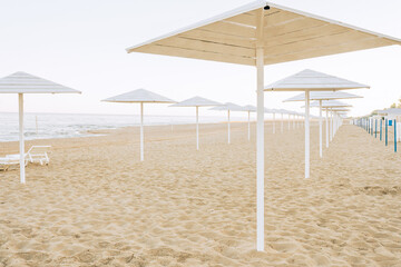 Empty sandy beach alond the sea with white umbrellas. Beach without tourists due to pandemic