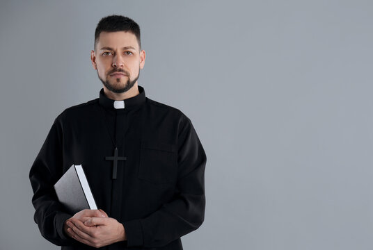 Priest with Bible on grey background, space for text