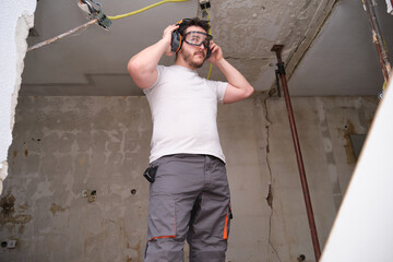 Young builder wearing hearing protection and safety glasses at a construction site. Safety at work.