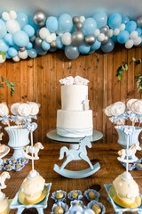 Decoração da mesa do bolo de festa de batismo e aniversário de menino com muitos doces diferentes, com tema de cavalinhos e anjinhos nas cores azul e branco.