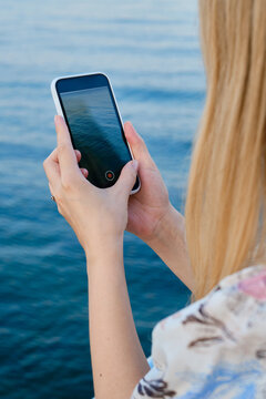 The girl holds a smart phone in her hands and takes pictures of the sea. Focus on the phone screen. Make memories using your smartphone. Mobile phone close up