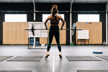 Obraz premium Young fitness woman doing barbell squats in a gym