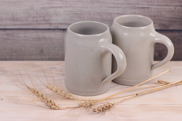 Two beer ceramic mugs with wheat ears on wooden background.German style.Brewing, octoberfest, St.Patrick's day, international beer day concept