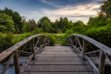 Fototapeta na wymiar Wooden Bridge over the pond on a walking path in a famous Stanley Park. Sunset Summer Sky. Downtown Vancouver, British Columbia, Canada.