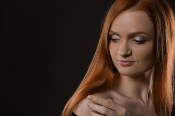 Fototapeta premium Portrait of happy young woman with charming smile and gorgeous red hair on dark background, space for text
