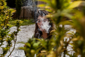 Young woman smoking next to a cannabis bush, homegrown.
