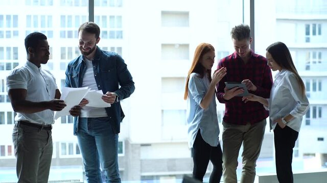 Successful young multi-ethnic startup business team having conversation in modern boardroom on background of window and skyscrapers. Portrait of serious multiethnic colleagues discuss project together
