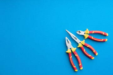 Technician's set of pliers on solid coloured blue background including pliers, long nose pliers and cutters