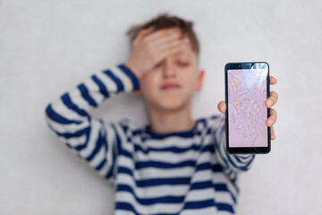 Unhappy and Sad boy holds a broken phone with cracks and colored spots in his hands. Selective...