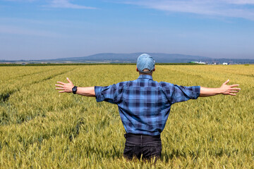 Farmer standing in a ripening wheat field looking at the sky above his head. Relationship between...