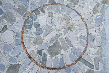 Top view of gray stone paved paving stones with a lined circle in the middle. The circle is separated by needles around the circumference.