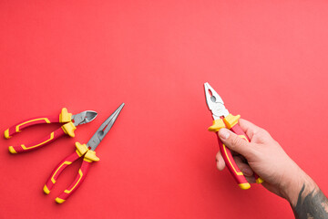 Technician's set of pliers on solid coloured red background including pliers, long nose pliers and cutters - obrazy, fototapety, plakaty
