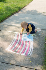 One year old baby next to chalk drawing of the American flag; toddler is crawling and playing with chalk on the 4th of July