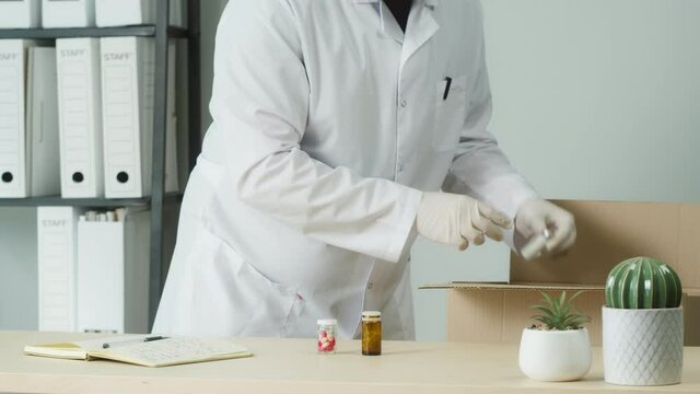 Doctor wearing medical mask and protective gloves taking medicine from box. Nurse unpacking drug medication delivery, pharmacist opening parcel and takes tablets and pills. Pharmacy shipping concept. 