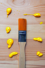 A synthetic bristle brush lies on wooden planks with drops of yellow acrylic paint, close-up.