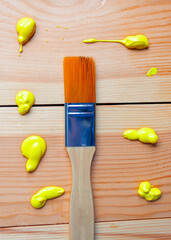 A synthetic bristle brush lies on wooden planks with drops of yellow acrylic paint. DIY repair