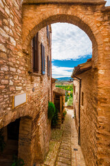 Spello charming historic center lane with stone arch and view of  Umbria countryside