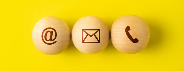 Contact us signs on wood ball spheres , symbols at, e-mail address and phone on yellow background.