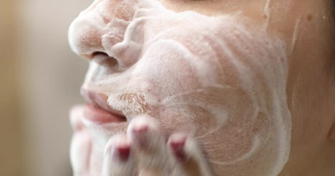 Young woman is washing applying foam cleanser on face. Daily facial skincare procedure.
