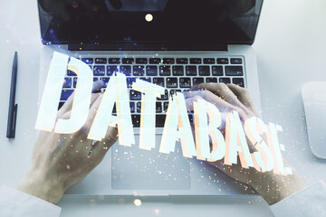 Double exposure of creative Database word hologram and hands typing on laptop on background, research and development concept