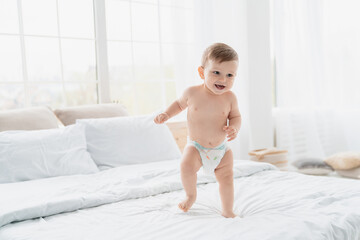 Small little caucasian baby newborn infant making first steps, cute toddler kid child girl son boy daughter learning walking creeping on the bed. Childcare and childhood concept - obrazy, fototapety, plakaty