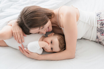 Young single mother embracing hugging her toddler newborn infant son daughter boy girl lying on bed together preparing for napping, singing lullaby and protecting her child. Motherhood and childcare