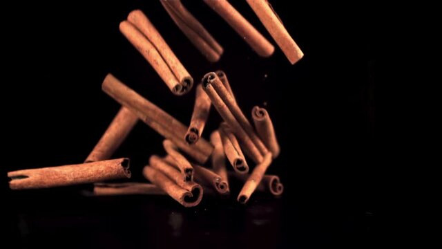 Super slow motion cinnamon sticks fall on the table in a heap. On a black background.Filmed on a high-speed camera at 1000 fps.
