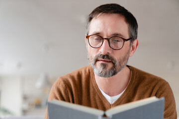 Relaxed pensive middle-aged mature man freelancer tutor adult student lecturer reading book at...