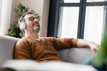 Tired mature man listening to the music in headphones lying on the sofa , enjoying sound tracks on social distance, isolation. Music fan concept, taking break.