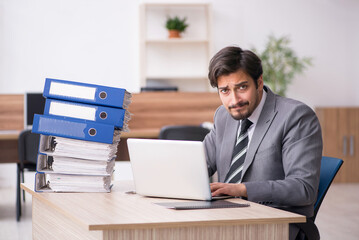 Fototapeta premium Young male employee unhappy with excessive work in the office